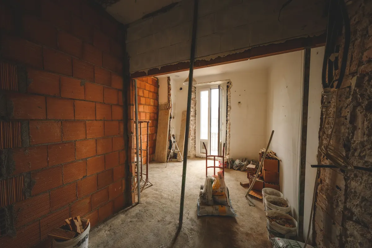 Pièce en cours de rénovation avec cloison en parpaings, outils et sacs de gravats